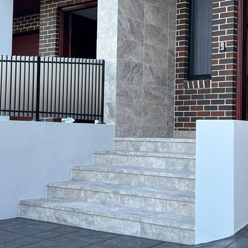 Front steps leading to a house with brick walls and travertine look tiles.