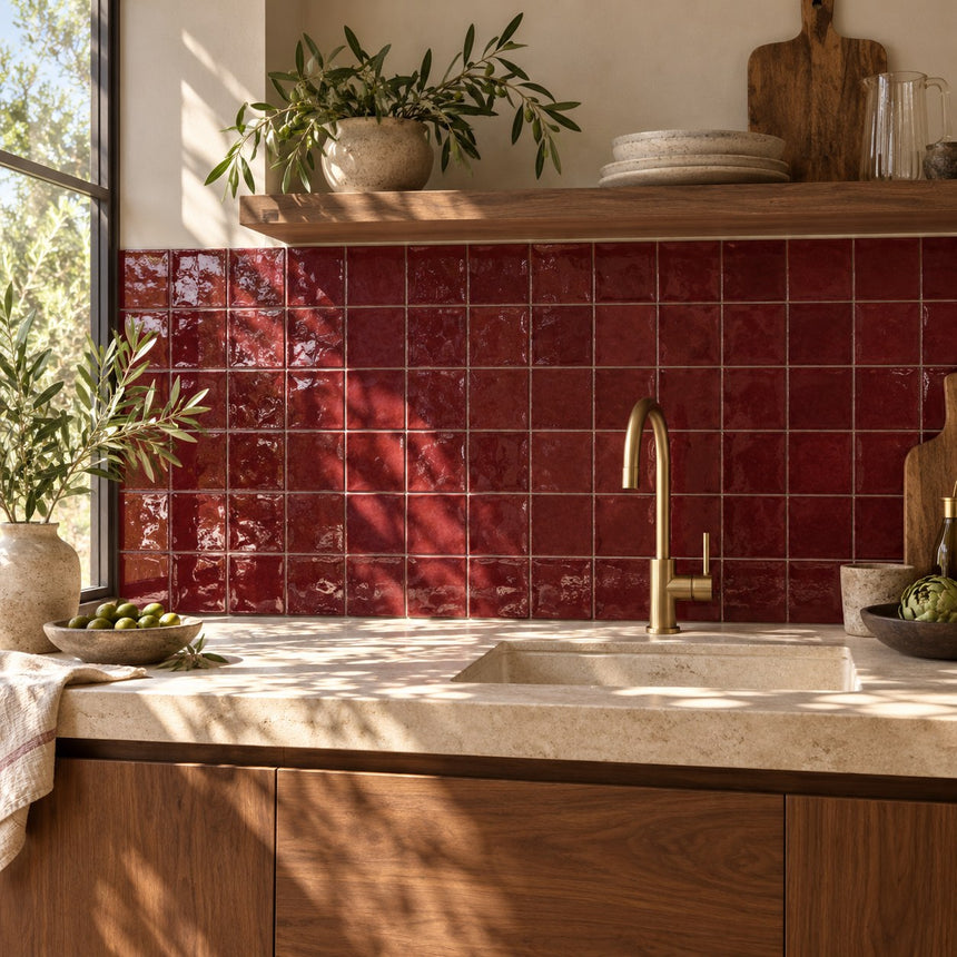 AI-generated illustrative kitchen with Majorca Burgundy gloss 100x100mm square wall tiles, sunlight, leafy tree shadows and green foliage. Confirm colour with a physical sample.